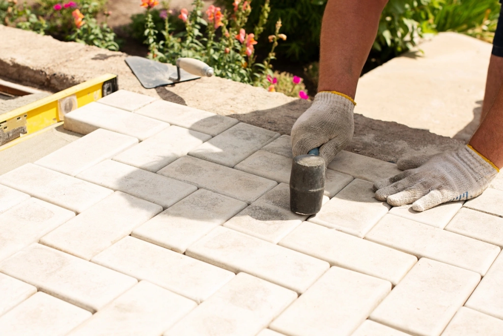 Un homme utilise un marteau en caoutchouc pour poser des pavés sur une terrasse de jardin